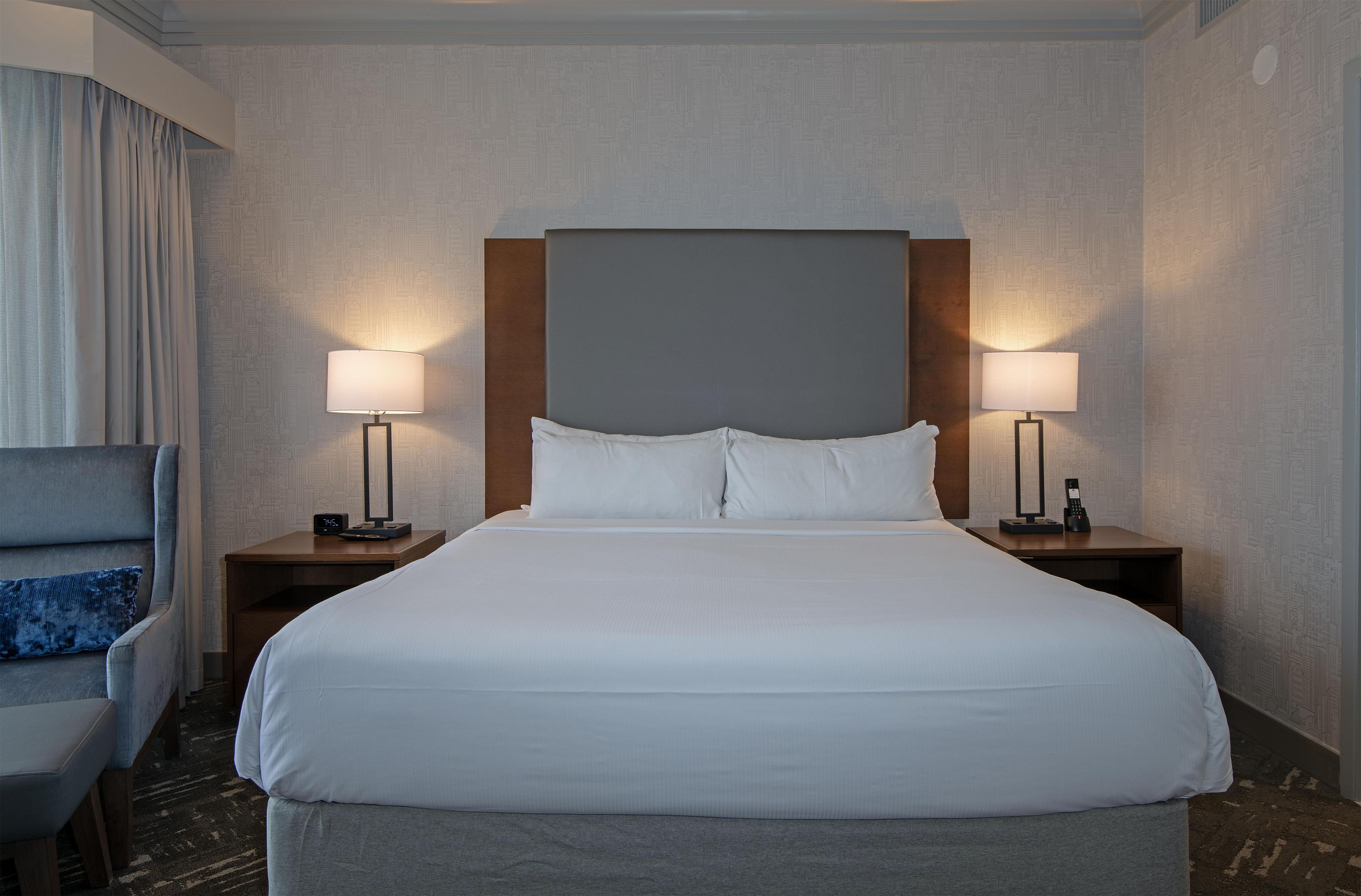 A hotel room with a large bed, two bedside tables, a chair, and a headboard.