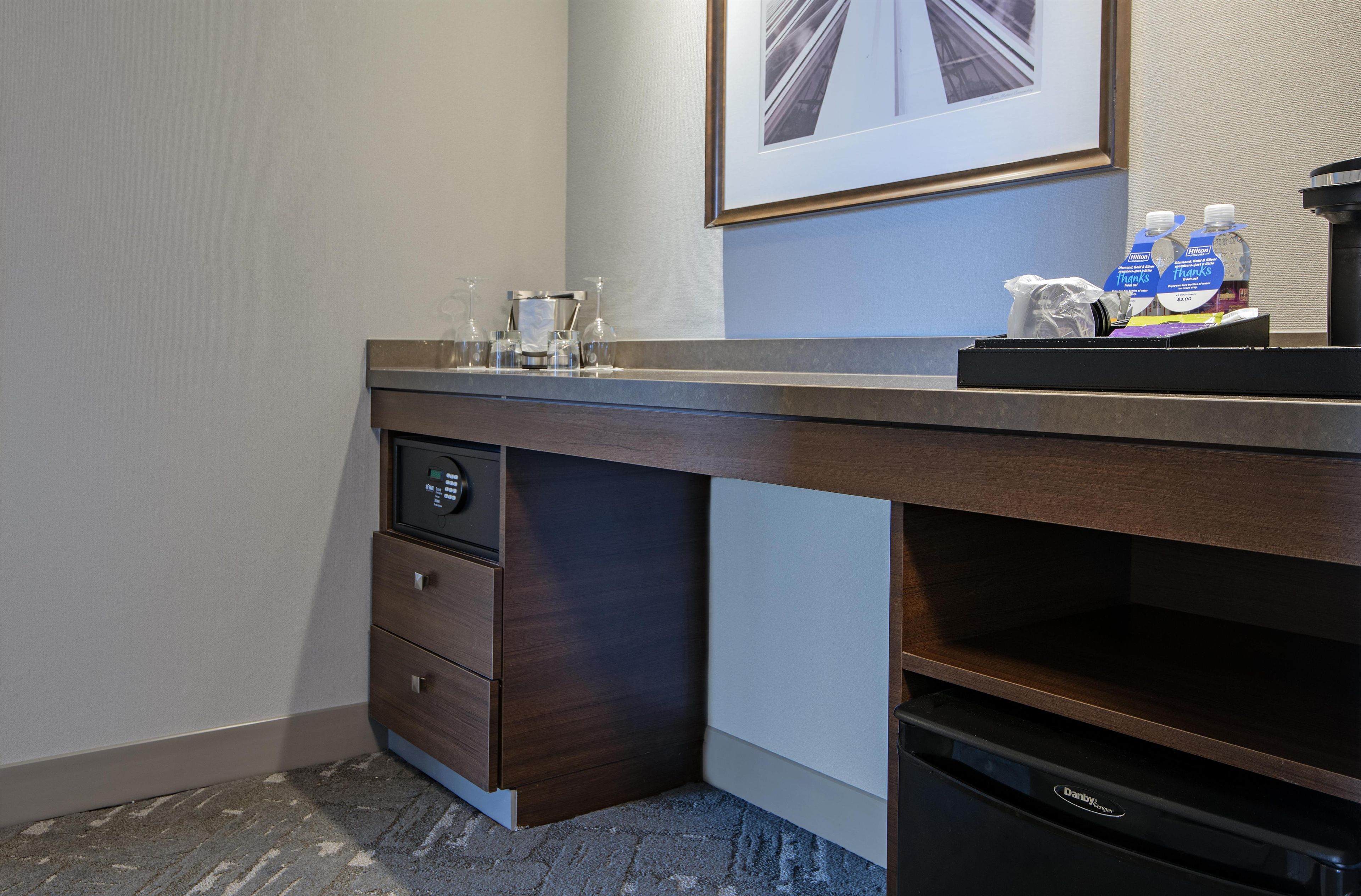 Habitación de hotel con escritorio de madera, cafetera, un cuadro enmarcado en la pared y un minibar.