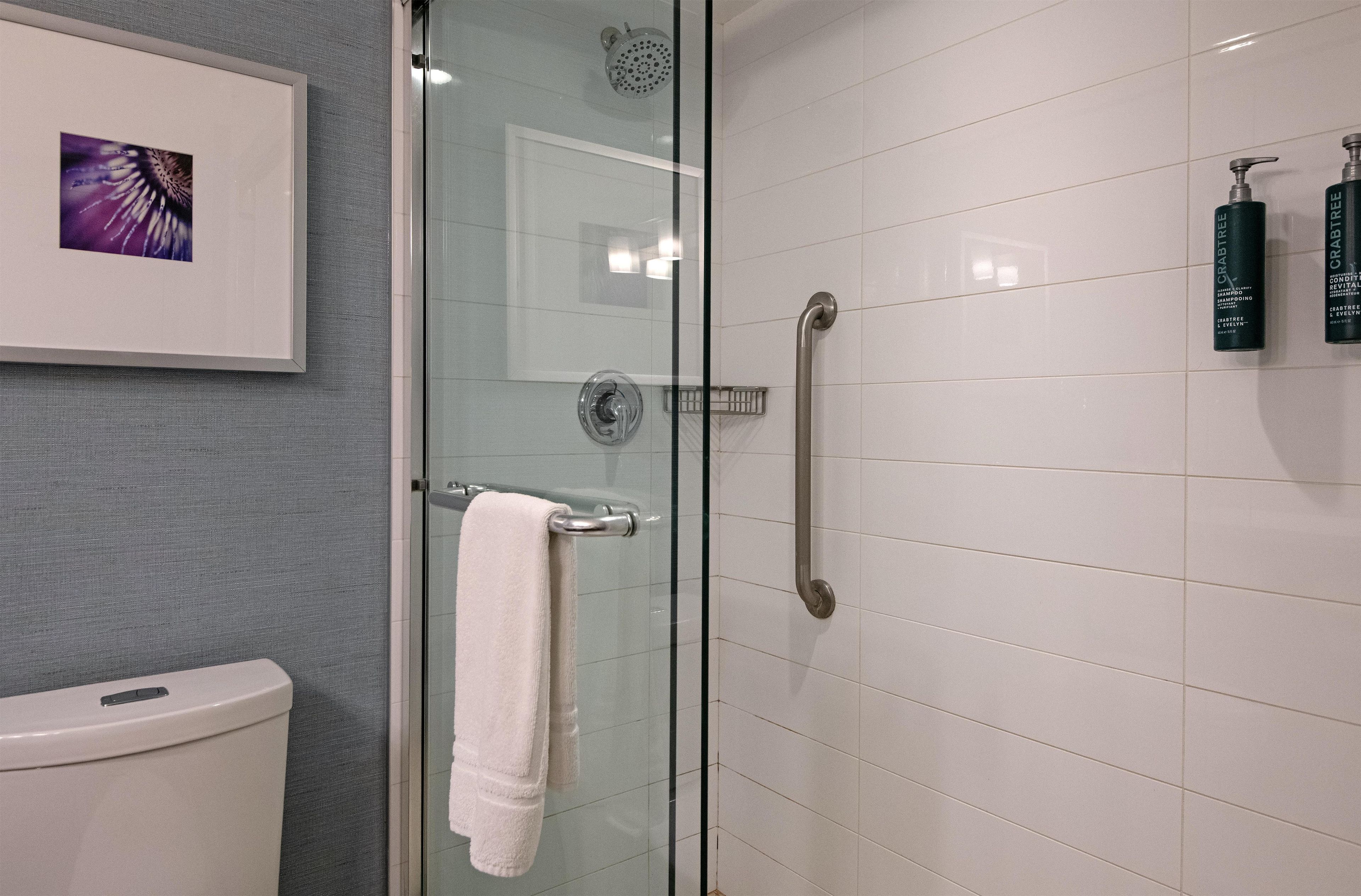 A bathroom with a glass shower enclosure, a white toilet, and two bottles of Crabtree brand shampoo on the wall.