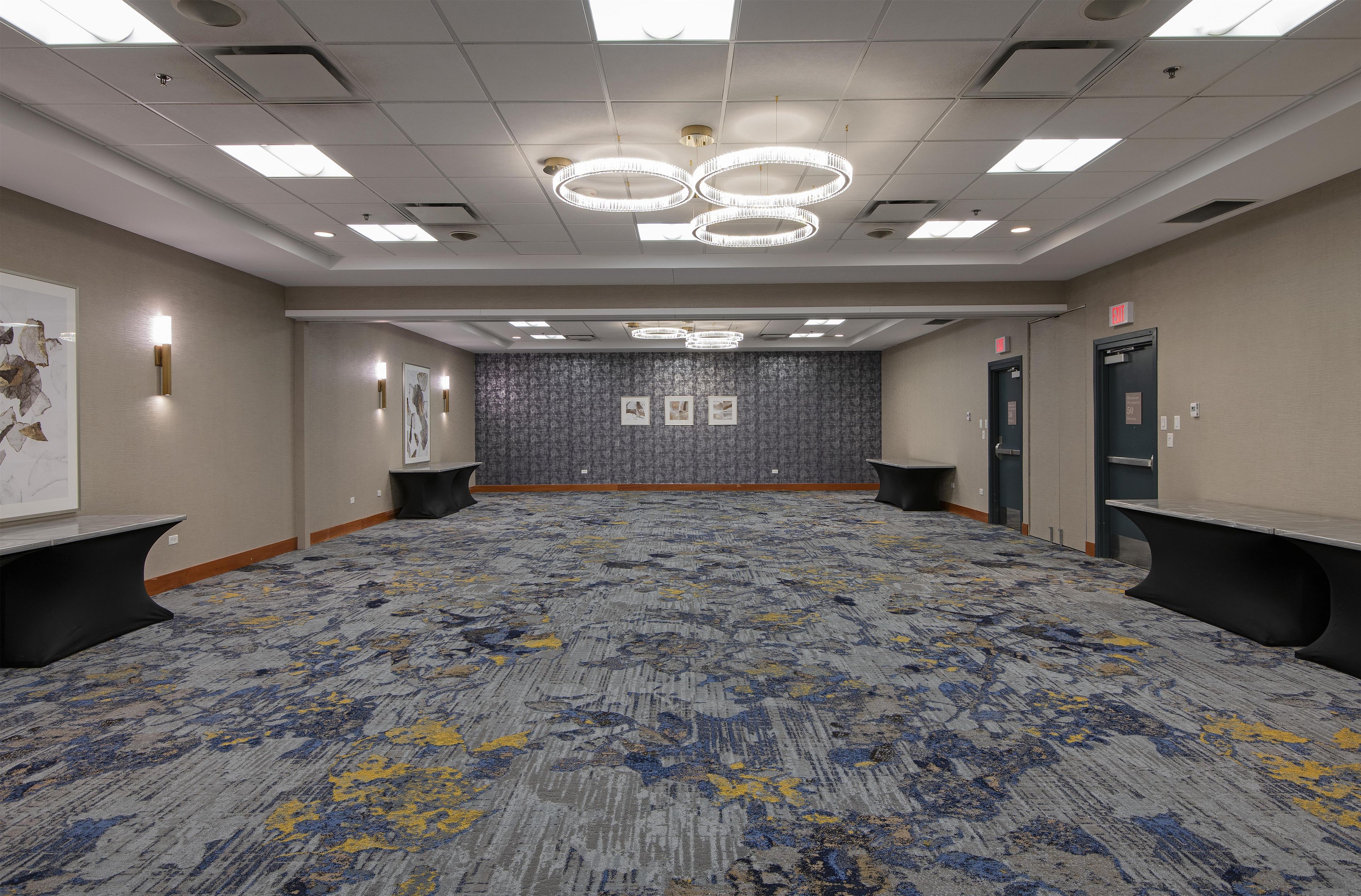 A large conference room with a patterned carpet, multiple exit signs, and a ceiling with recessed lighting and chandeliers.