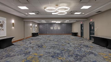 A large conference room with a patterned carpet, multiple exit signs, and a ceiling with recessed lighting and chandeliers.
