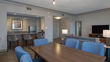 Una habitación de hotel con una mesa de comedor, taburetes de bar, un sofá, un televisor y una lámpara.