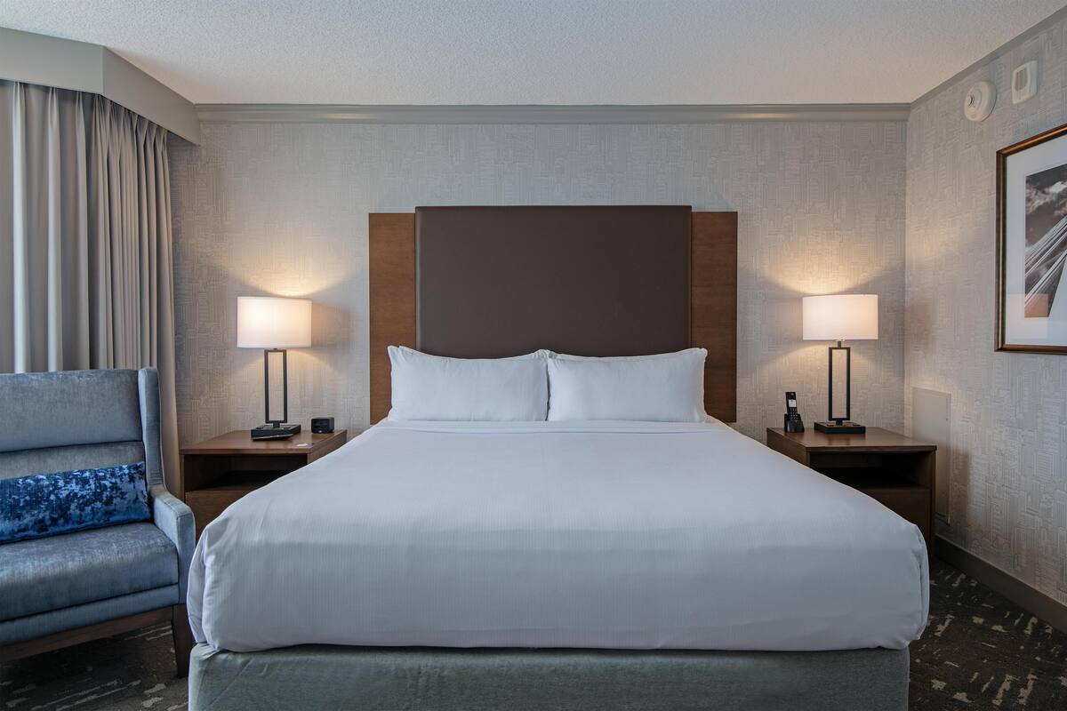 A hotel room with a large bed, two bedside tables with lamps, a chair, and a framed picture on the wall.
