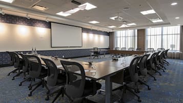 A conference room with a long table, chairs, a projector screen, and a large window.