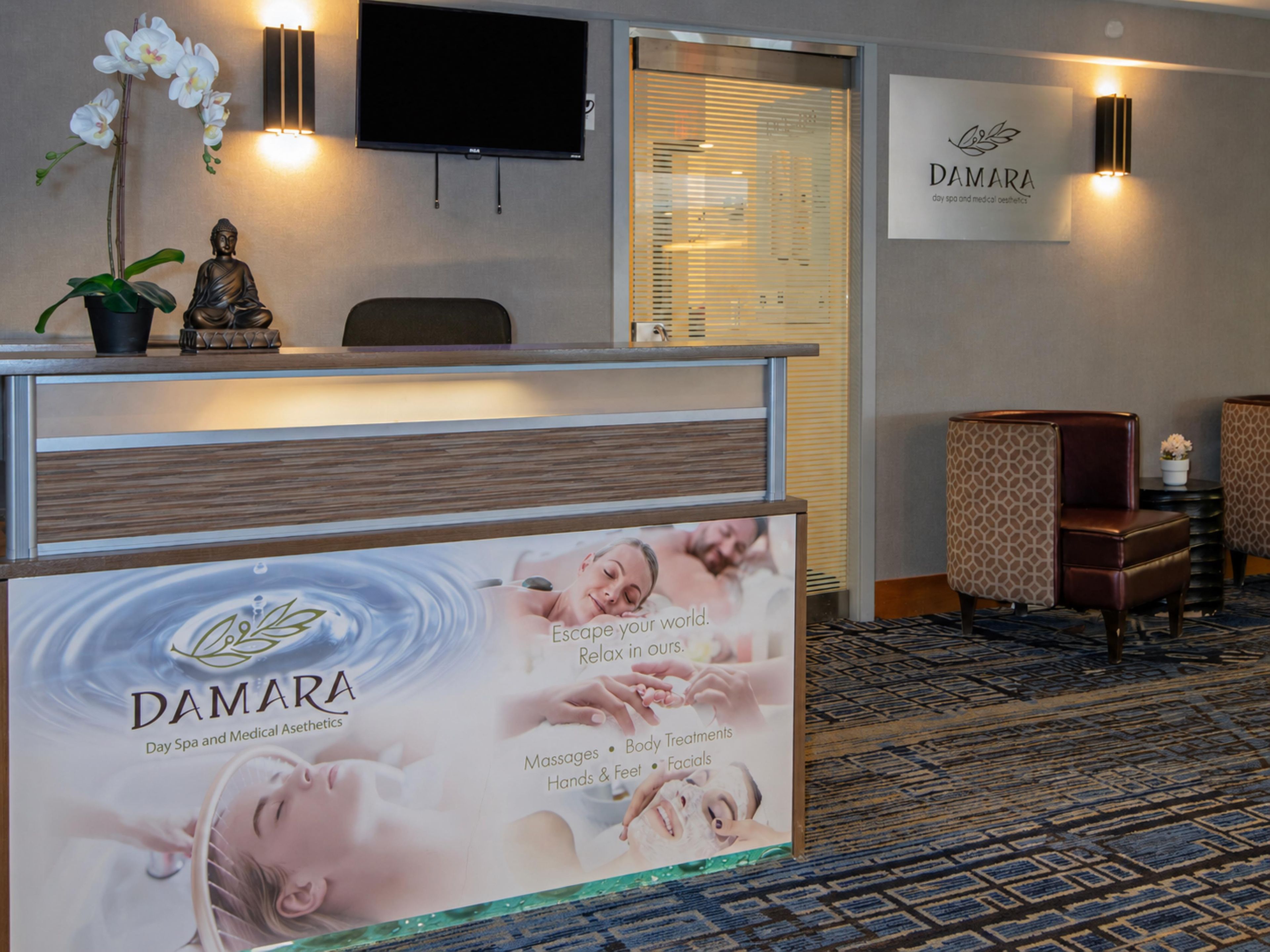 Zona de recepción con mostrador, estatua de Buda, televisor y un letrero en la pared para DAMARA Day Spa y Medical Aesthetics.