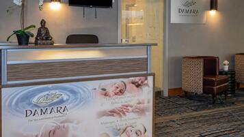 Zona de recepción con mostrador, estatua de Buda, televisor y un letrero en la pared para DAMARA Day Spa y Medical Aesthetics.