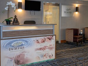 A reception area with a reception desk, a Buddha statue, a TV, and a wall-mounted sign for DAMARA Day Spa and Medical Aesthetics. - DoubleTree by Hilton Hotel West Edmonton (Edmonton)