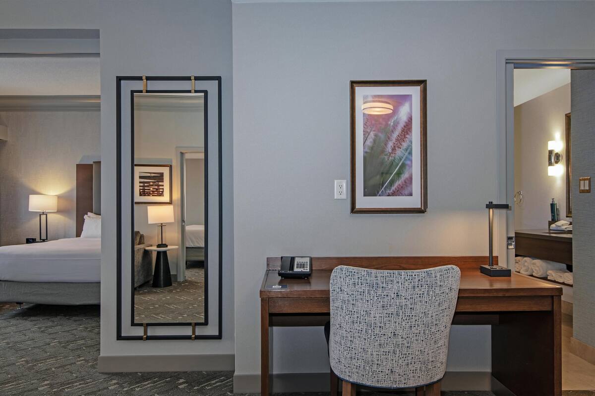 A hotel room with a bed, desk, chair, and a large mirror.