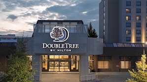 Entrada de un hotel DoubleTree by Hilton con logotipo de árbol, cielo despejado y estacionamiento.