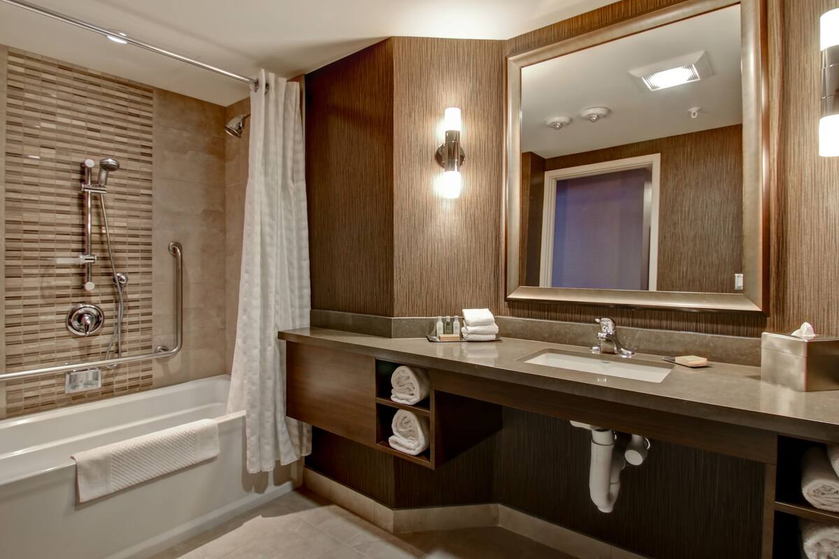 A modern bathroom with a bathtub, shower, vanity with a mirror, and towel storage.