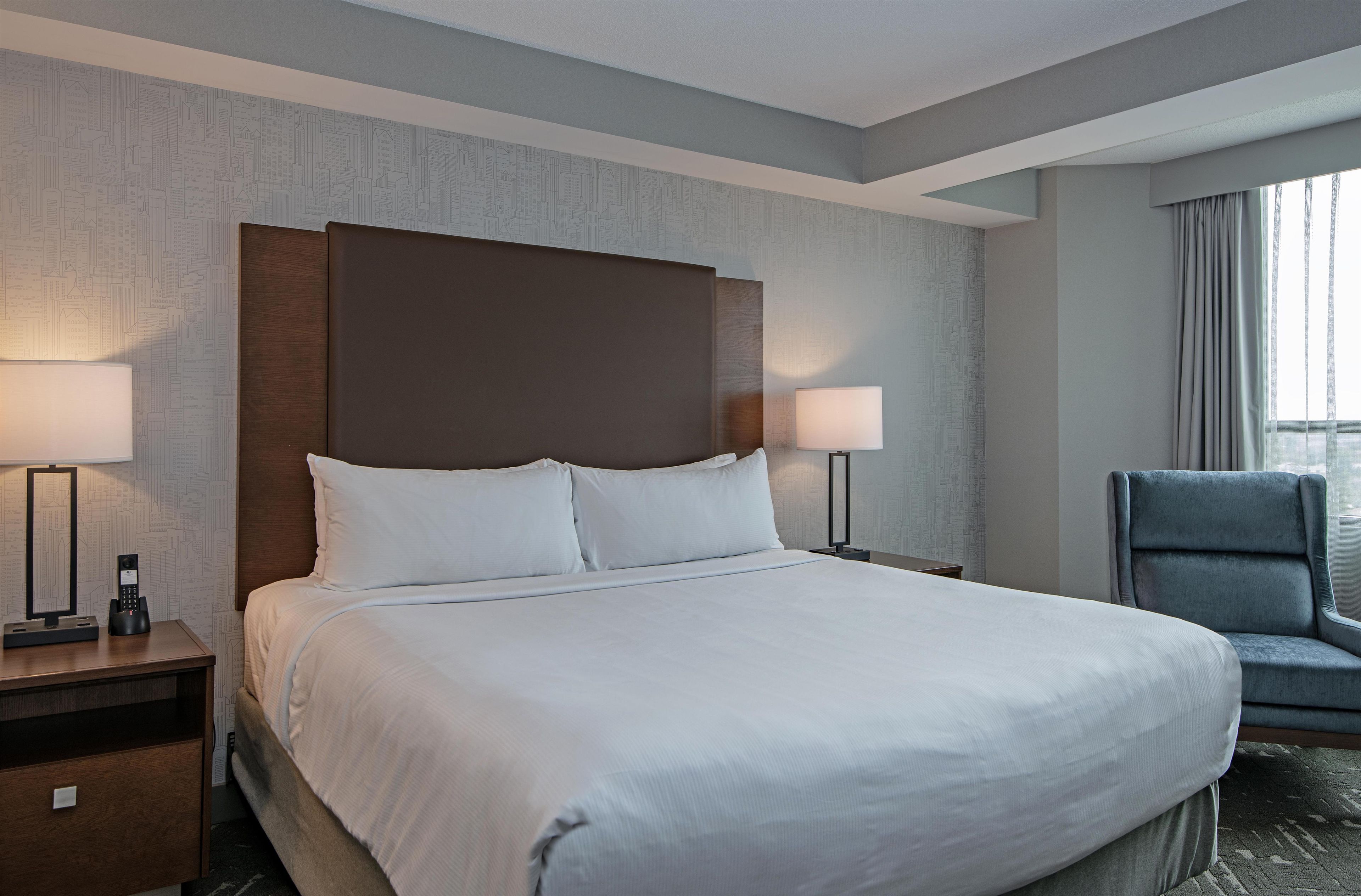 A hotel room with a large bed, two bedside lamps, a chair, and a window with curtains.