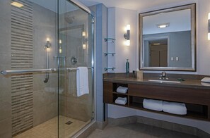 Ein modernes Badezimmer mit einer gläsernen Duschkabine, einem großen Spiegel und einem Holzwaschtisch mit Ablageflächen.