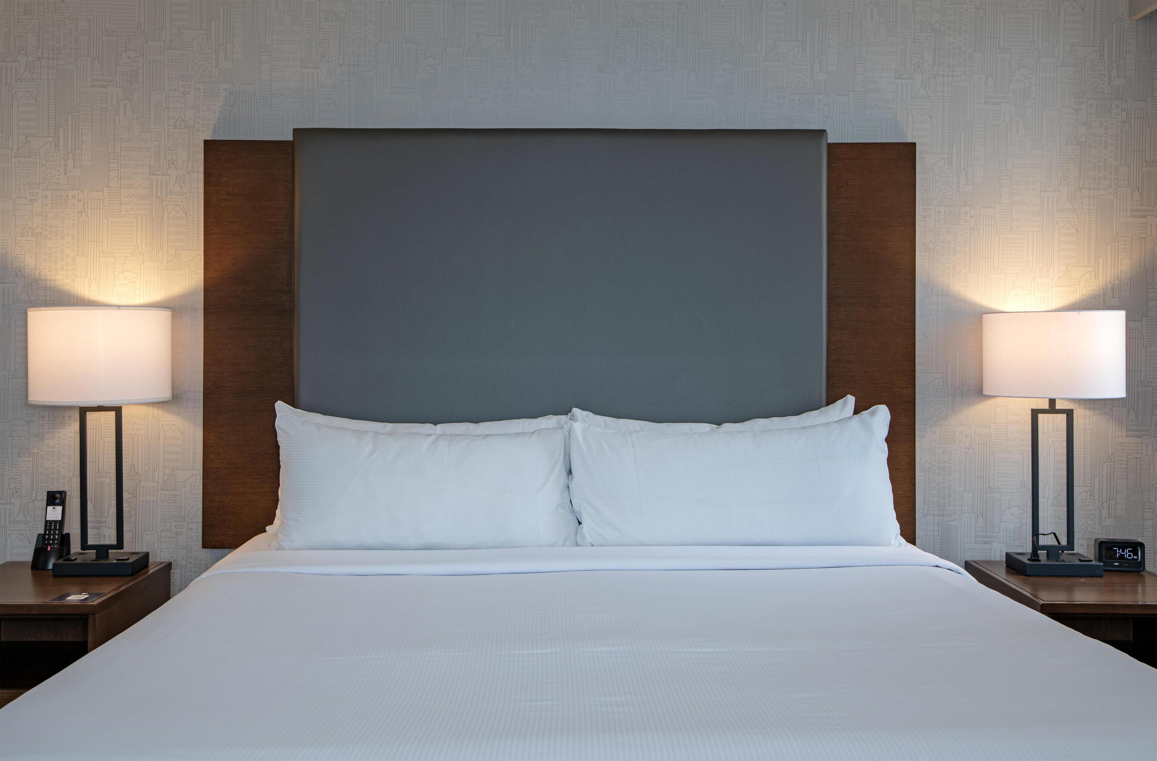 A hotel room with a large bed, two bedside tables, a nightstand, a wall clock, and a patterned wallpaper.