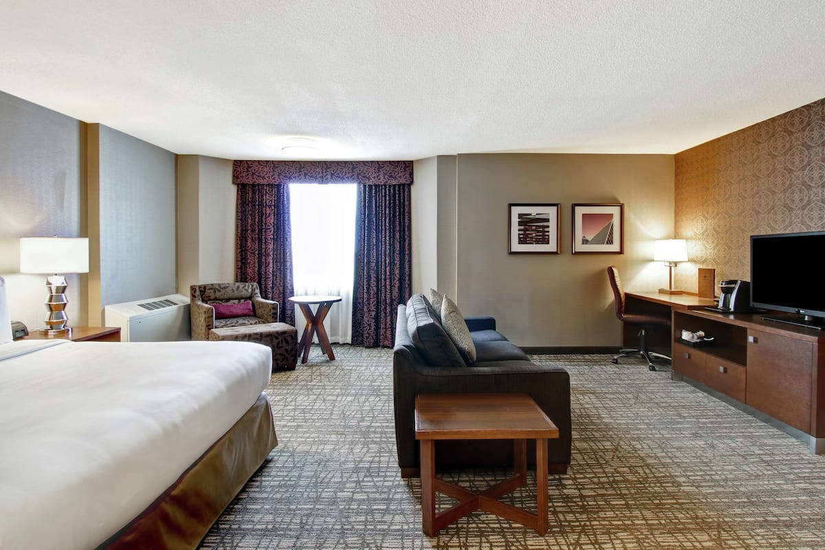 A hotel room with a bed, sofa, desk, TV, and two framed pictures on the wall.