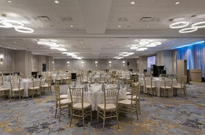 A large banquet hall with round tables and chairs, recessed lighting, and a stage area. - DoubleTree by Hilton Hotel West Edmonton (Edmonton)