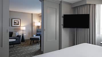 A hotel room with a bed, a TV mounted on the wall, a desk, a chair, a lamp, and a framed picture on the wall.
