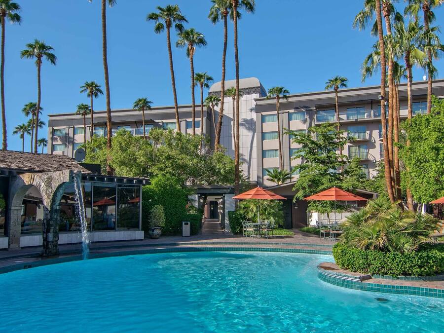 Un hotel con piscina, palmeras y un edificio con balcones.