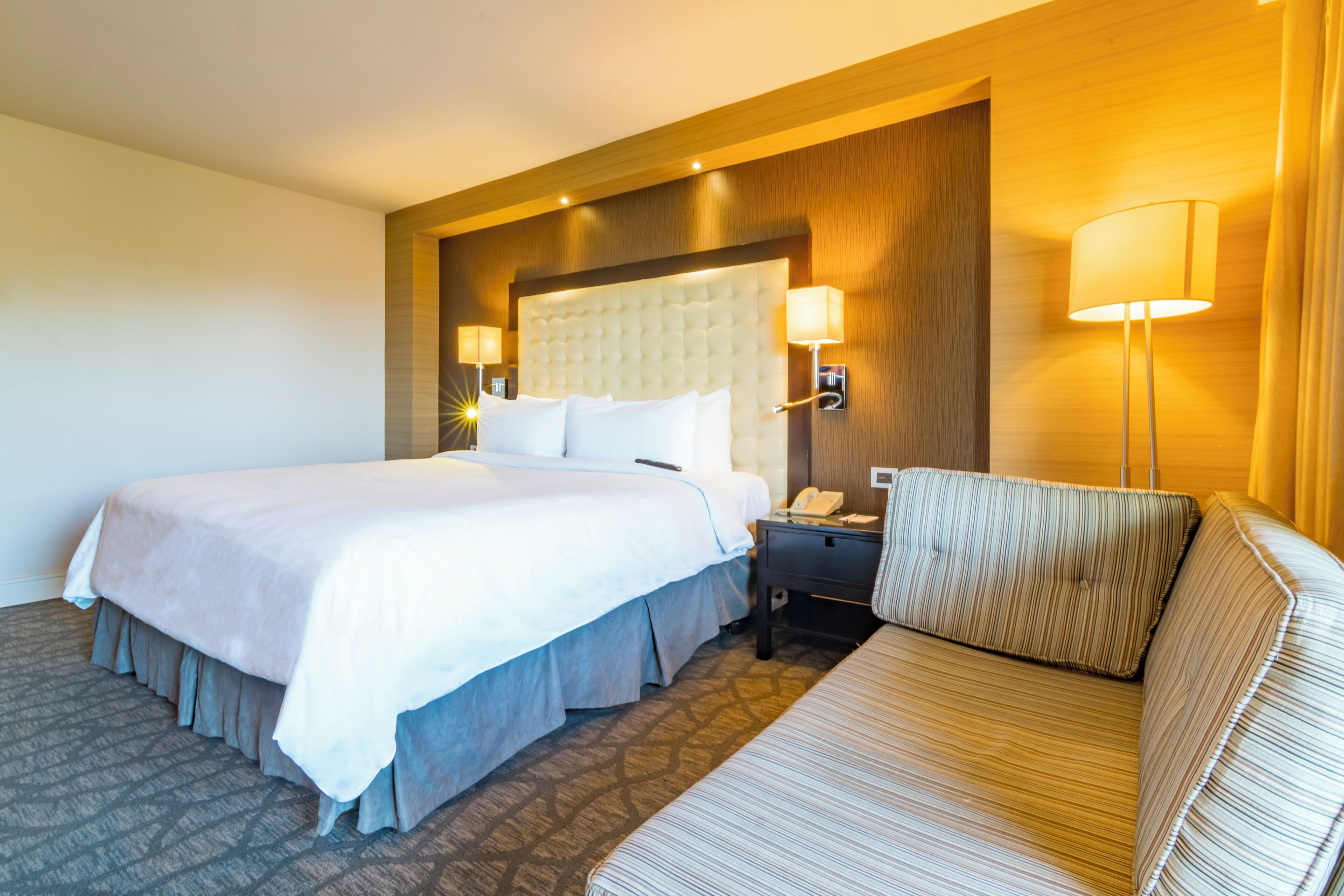 A hotel room with a large bed, a bedside table with a lamp, and a sofa.