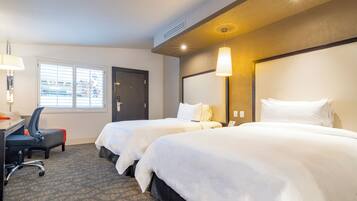 A hotel room with two beds, a desk with a chair, and a window with blinds.