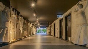 A corridor with stone sculptures on the walls, a tiled floor, and a sign indicating restrooms. - Hotel Lucerna Mexicali (Mexicali)