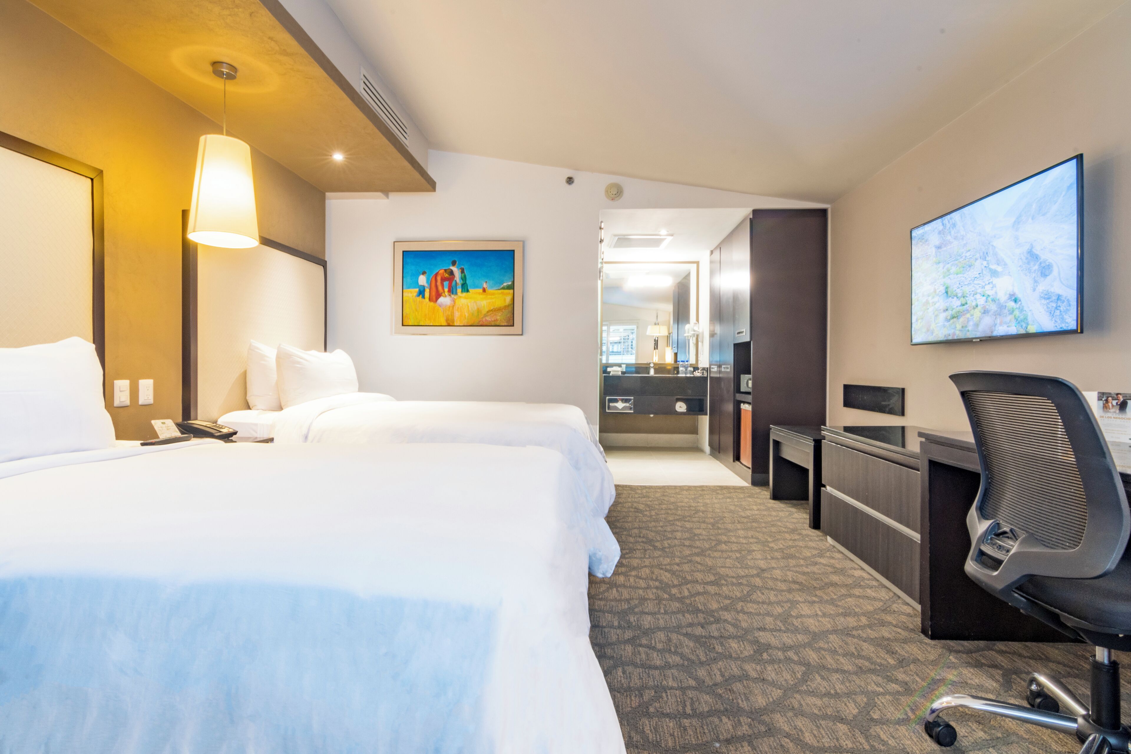 A hotel room with two beds, a desk, a chair, a TV, and a painting on the wall.