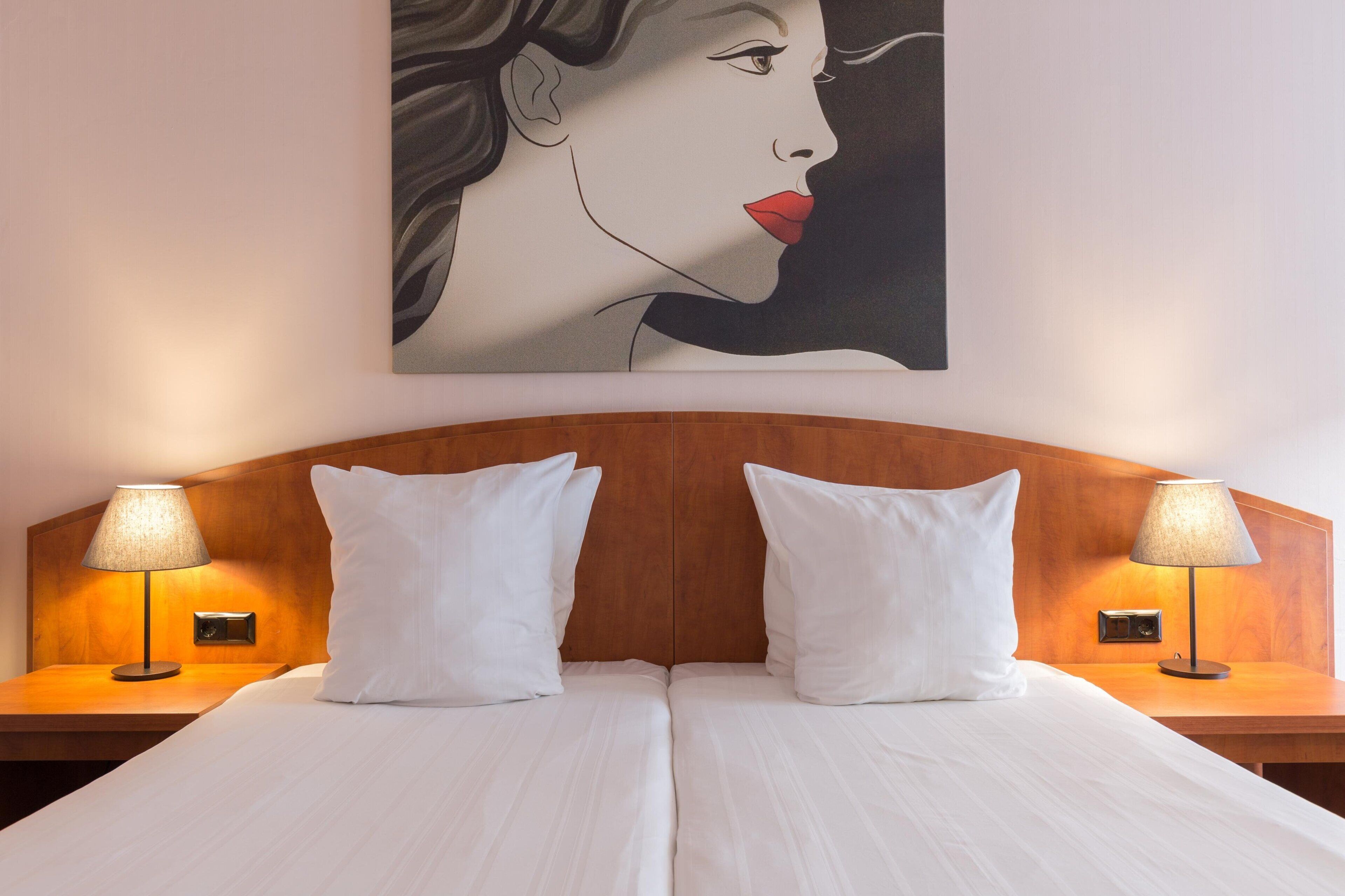 A double bed with white linens, two bedside lamps, and a wooden headboard.