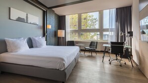 A hotel room with a large bed, a desk, a chair, and a window with curtains. - Leonardo Hotel Utrecht City Center (Utrecht)