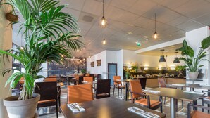 A modern restaurant with high tables and chairs, potted plants, and pendant lighting. - Leonardo Hotel Utrecht City Center (Utrecht)