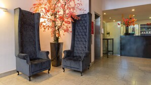 A reception area with two upholstered chairs, a potted plant with red foliage, and a bar area in the background. - Leonardo Hotel Utrecht City Center (Utrecht)
