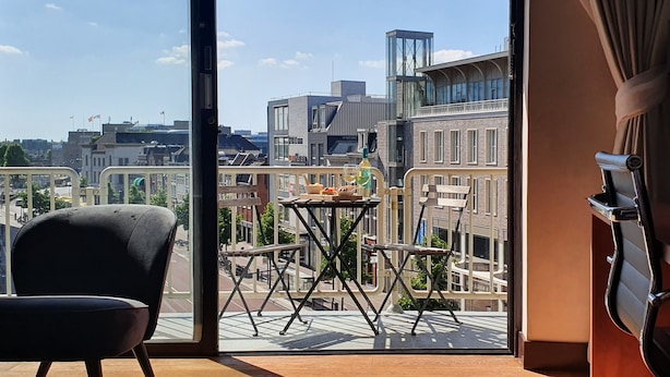 A balcony with a view of the city, a table with chairs, and a black chair inside. - Leonardo Hotel Utrecht City Center (Utrecht)