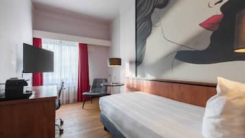 A hotel room with a bed, desk, chair, television, and a large painting on the wall.