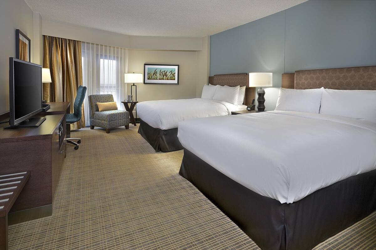 A hotel room with two beds, a desk, a television, and a chair.