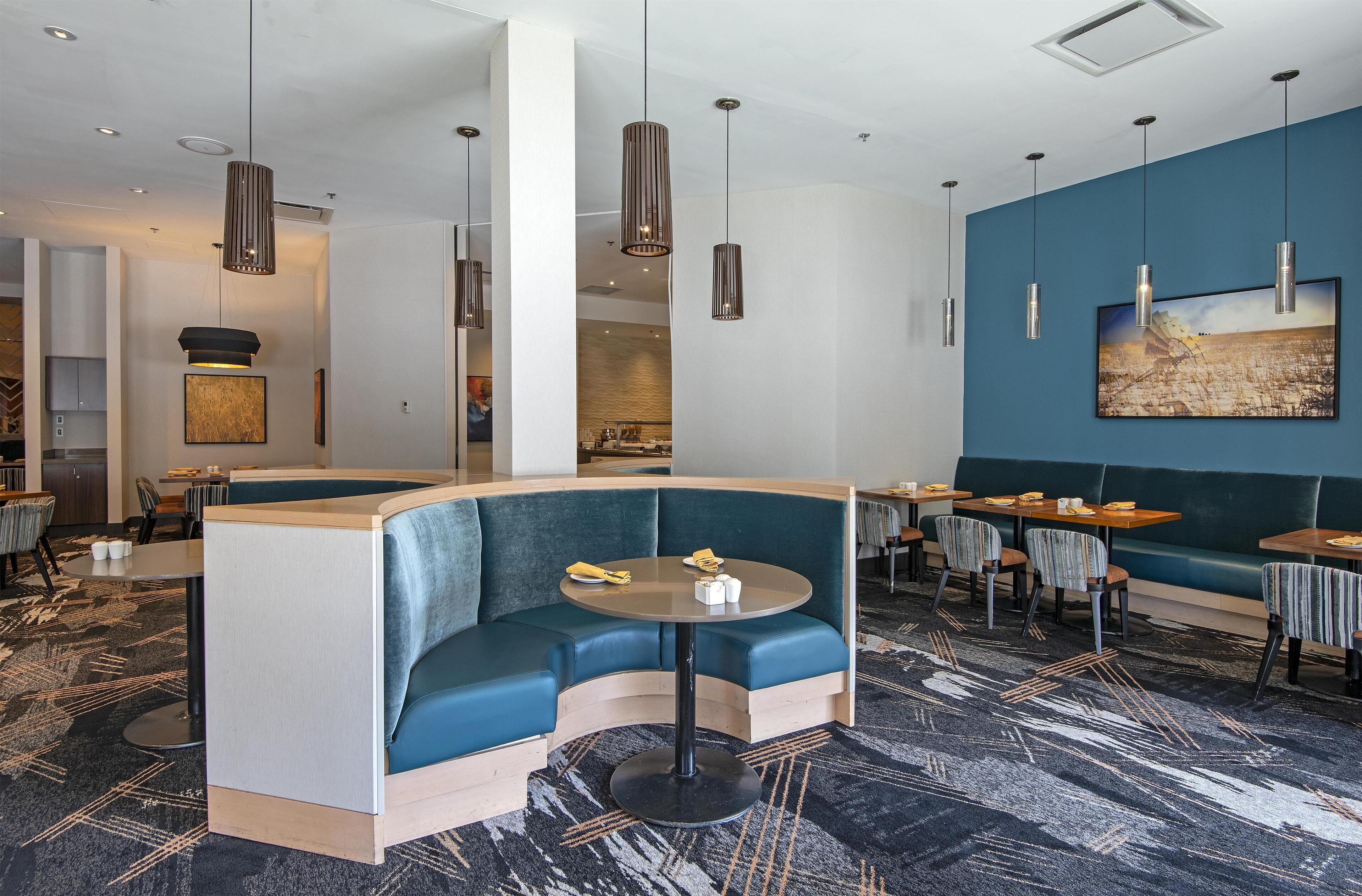 A modern restaurant with a curved seating area, pendant lighting, and a large painting on the wall.