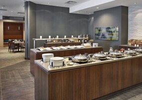 Un área de bufé con varias estaciones de servicio, una zona de estar con mesas y sillas, y una pared decorativa con un diseño texturizado.