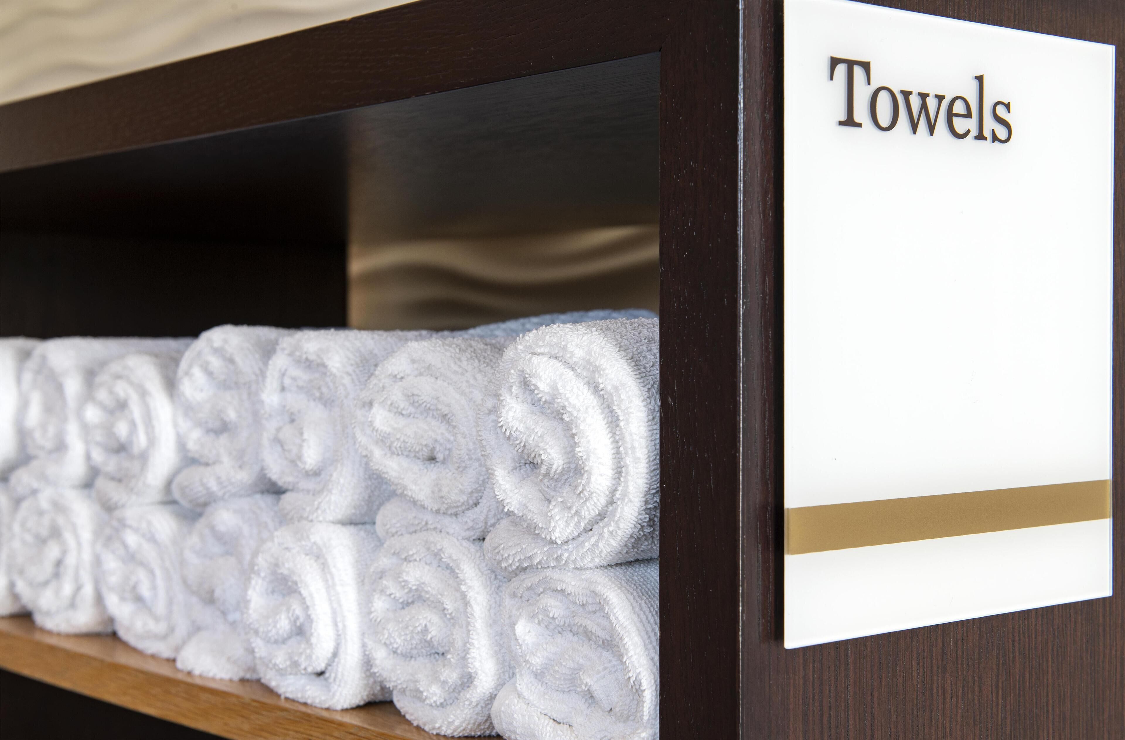 A neatly arranged shelf with rolled white towels and a sign labeled "Towels".