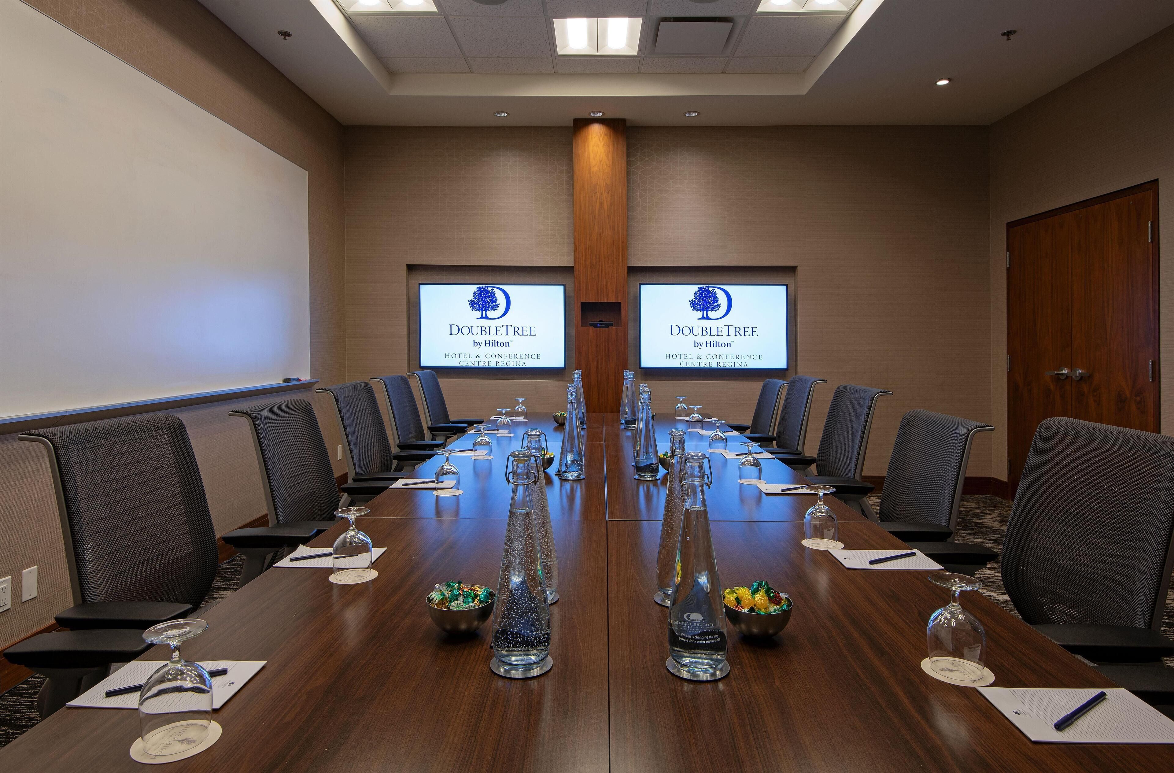 A conference room with a long table, chairs, and a projector screen displaying the DoubleTree logo.