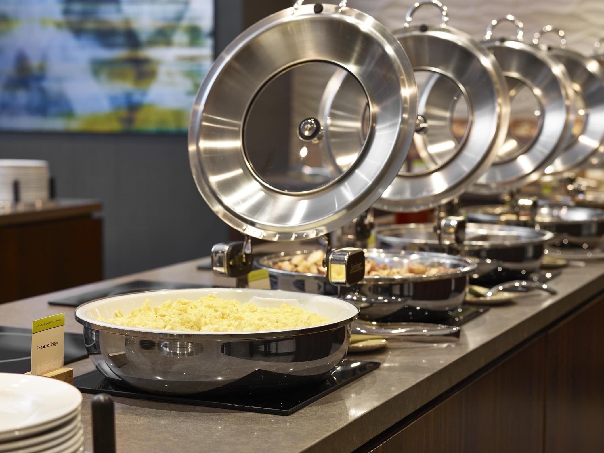 A buffet setup with multiple covered serving dishes, including scrambled eggs, arranged on a counter.