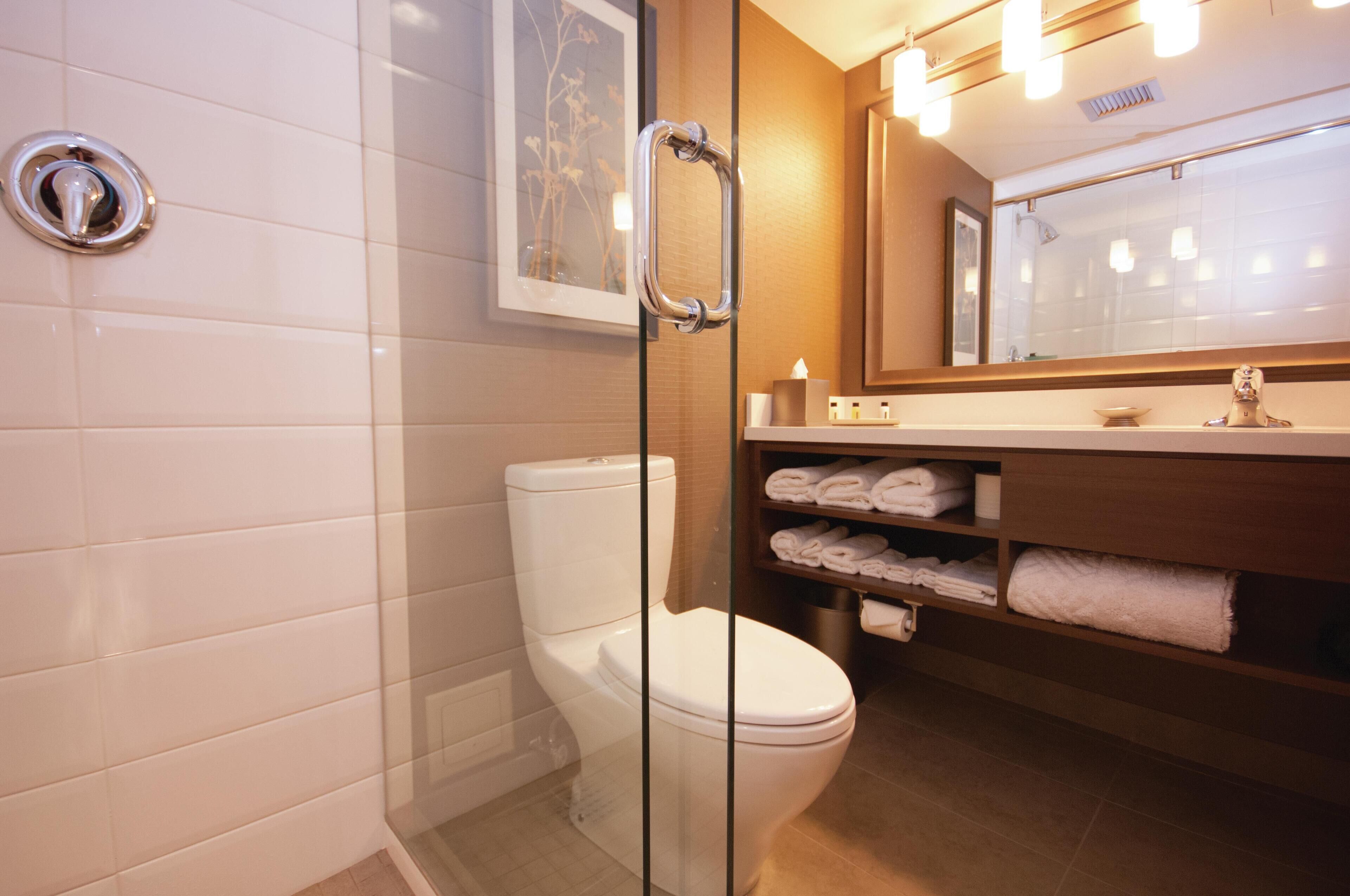 A modern bathroom with a glass shower enclosure, a white toilet, and a wooden vanity with neatly folded towels.