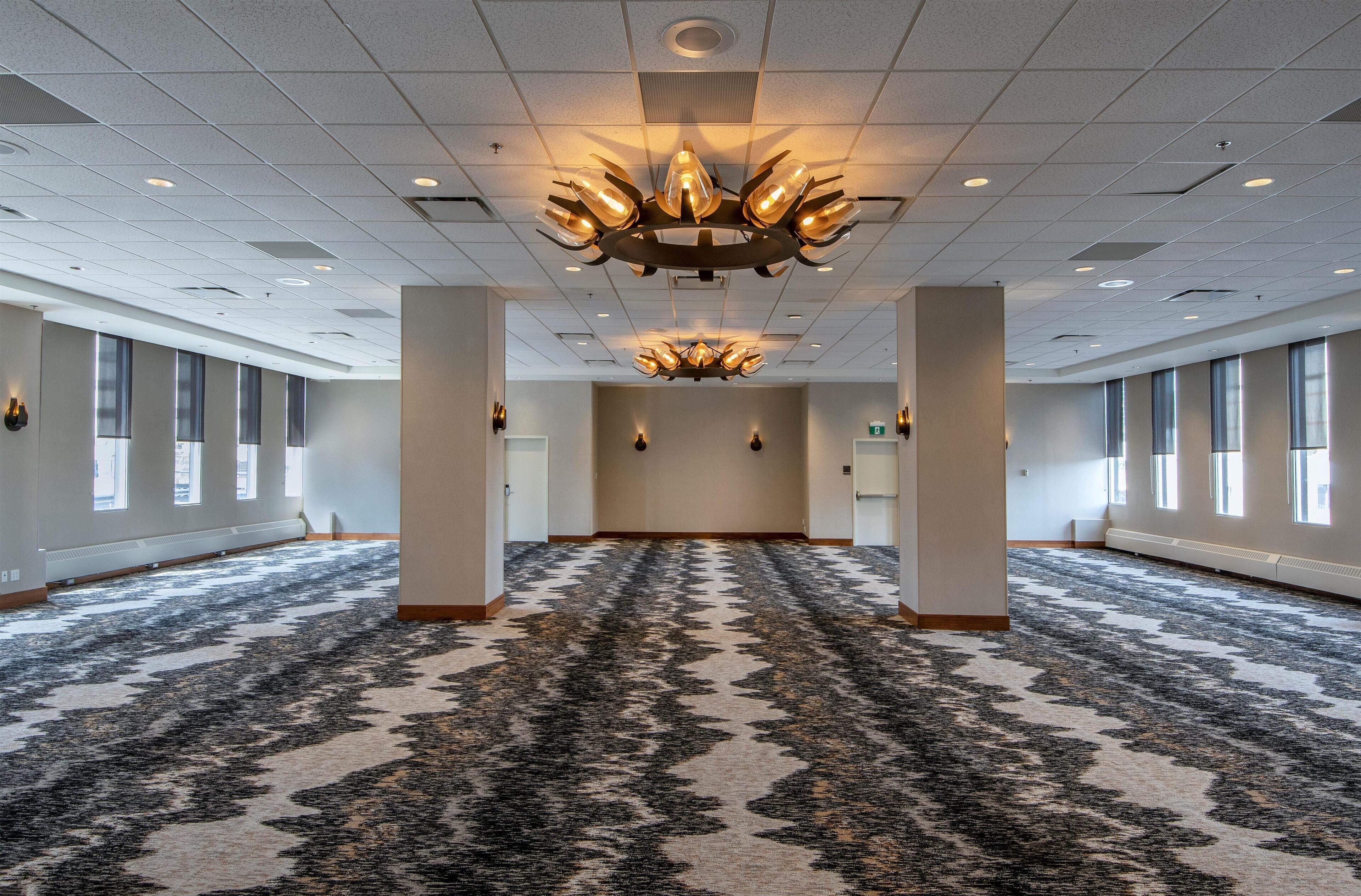 A spacious, well-lit conference room with a patterned carpet, large windows, and a modern chandelier.