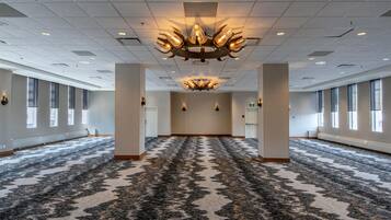 A spacious, well-lit conference room with a patterned carpet, large windows, and a modern chandelier.