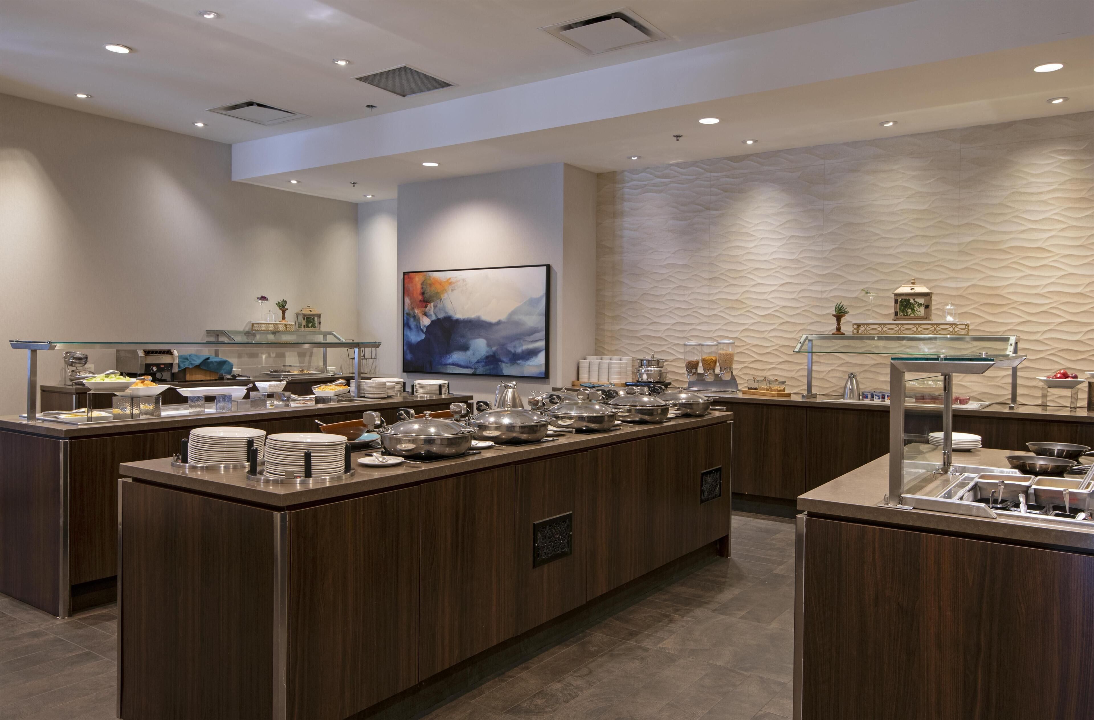 A modern breakfast bar with multiple serving stations, a large abstract painting, and a textured wall.
