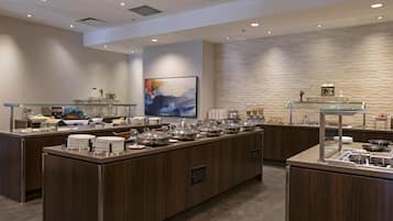 A modern breakfast bar with multiple serving stations, a large abstract painting, and a textured wall.