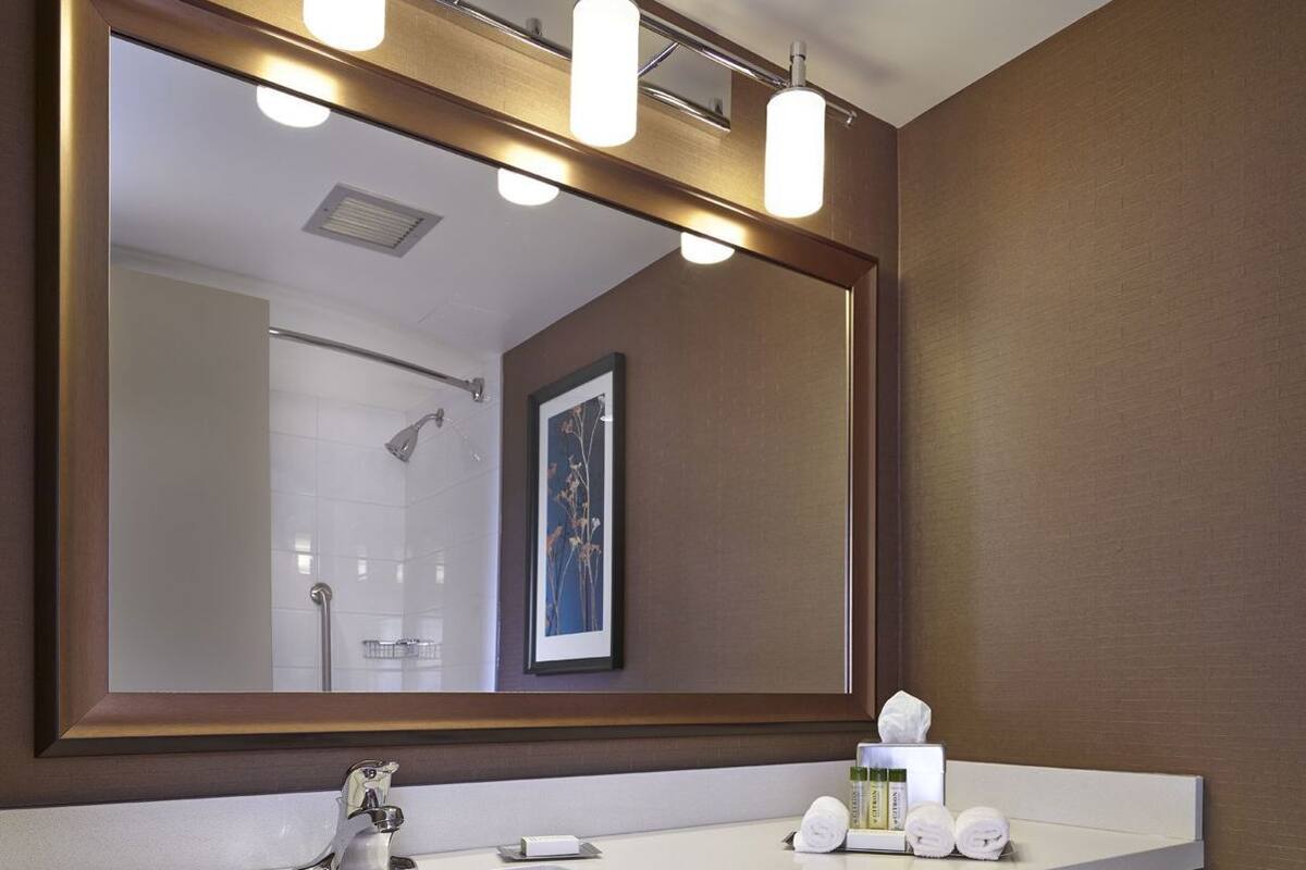 A bathroom with a large mirror, a sink, and shelves with towels.