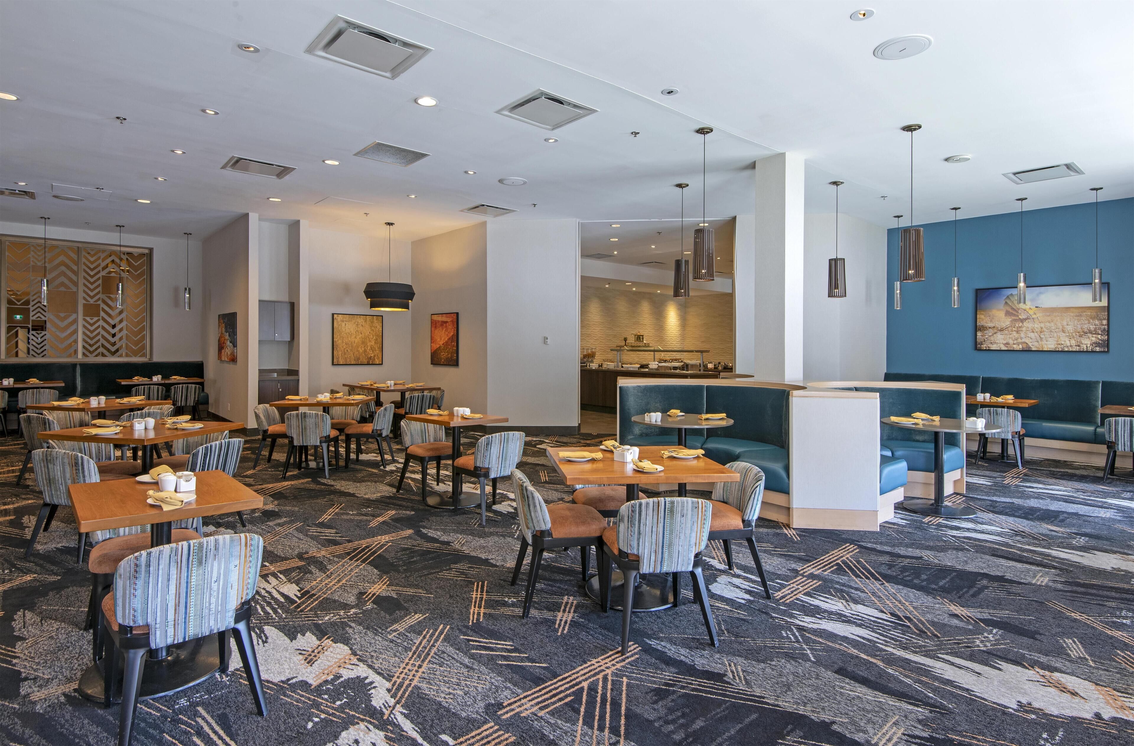 Un restaurant d’hôtel doté de nombreuses tables et chaises, d’un bar et offrant une vue sur la cuisine.