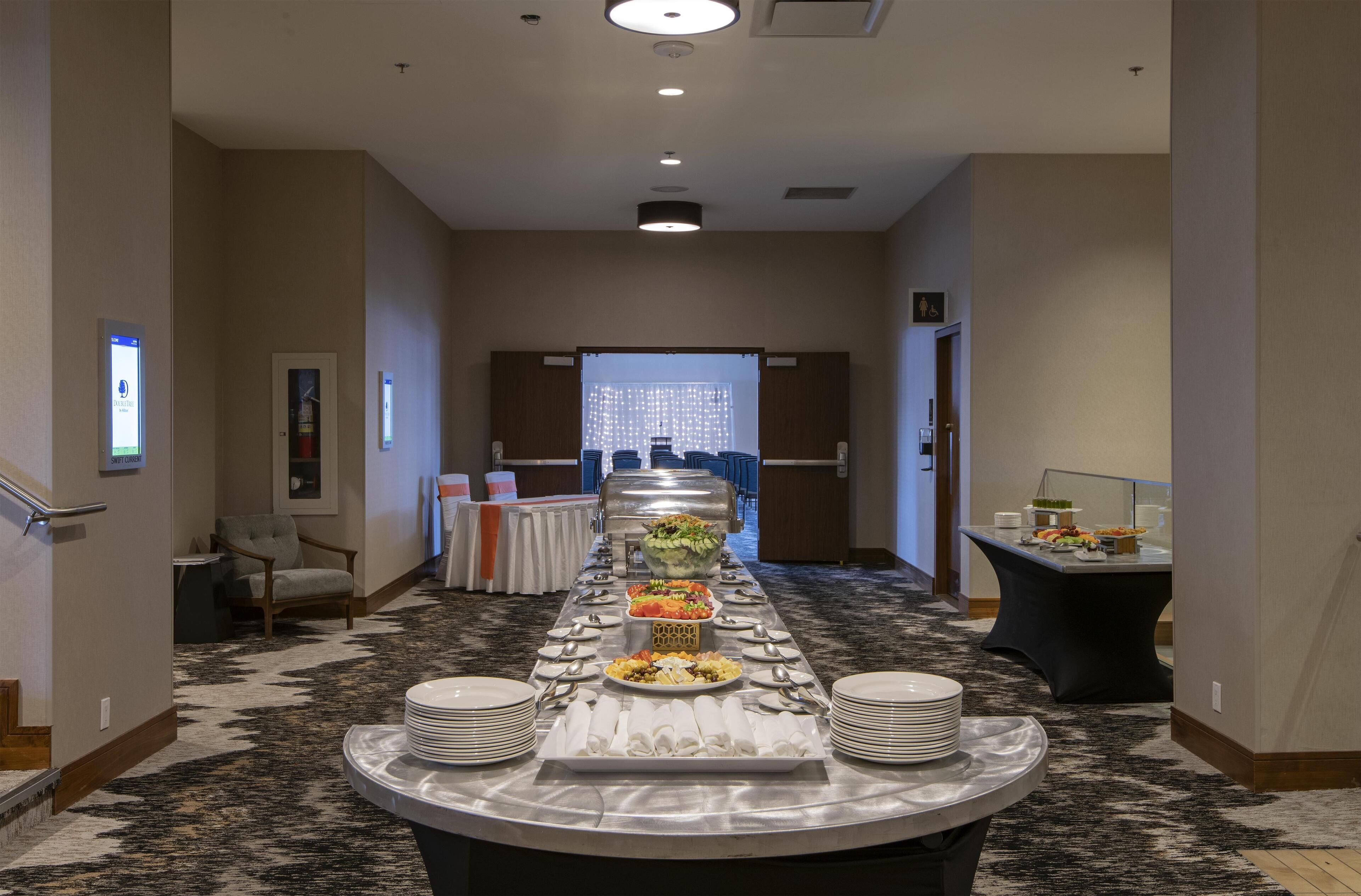 Pasillo de hotel con una mesa de buffet en el centro, que presenta diferentes alimentos y utensilios.