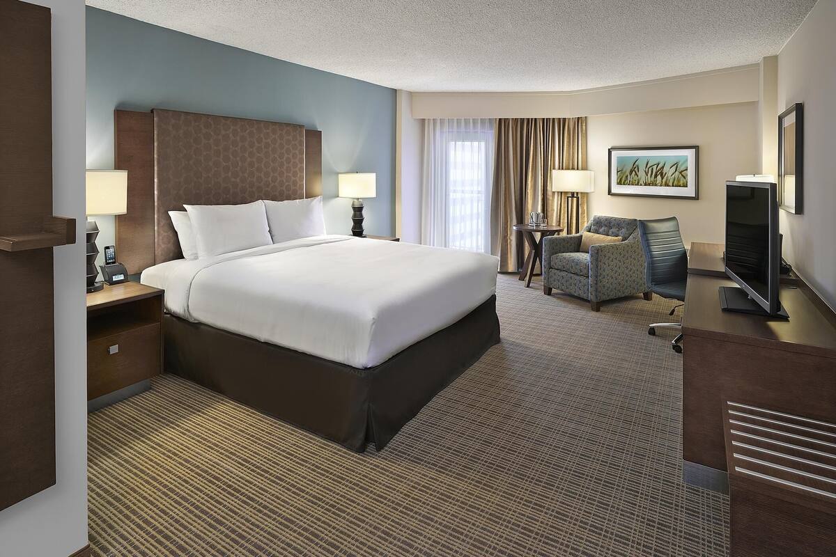 A hotel room with a large bed, a desk with a computer, a chair, and a television.