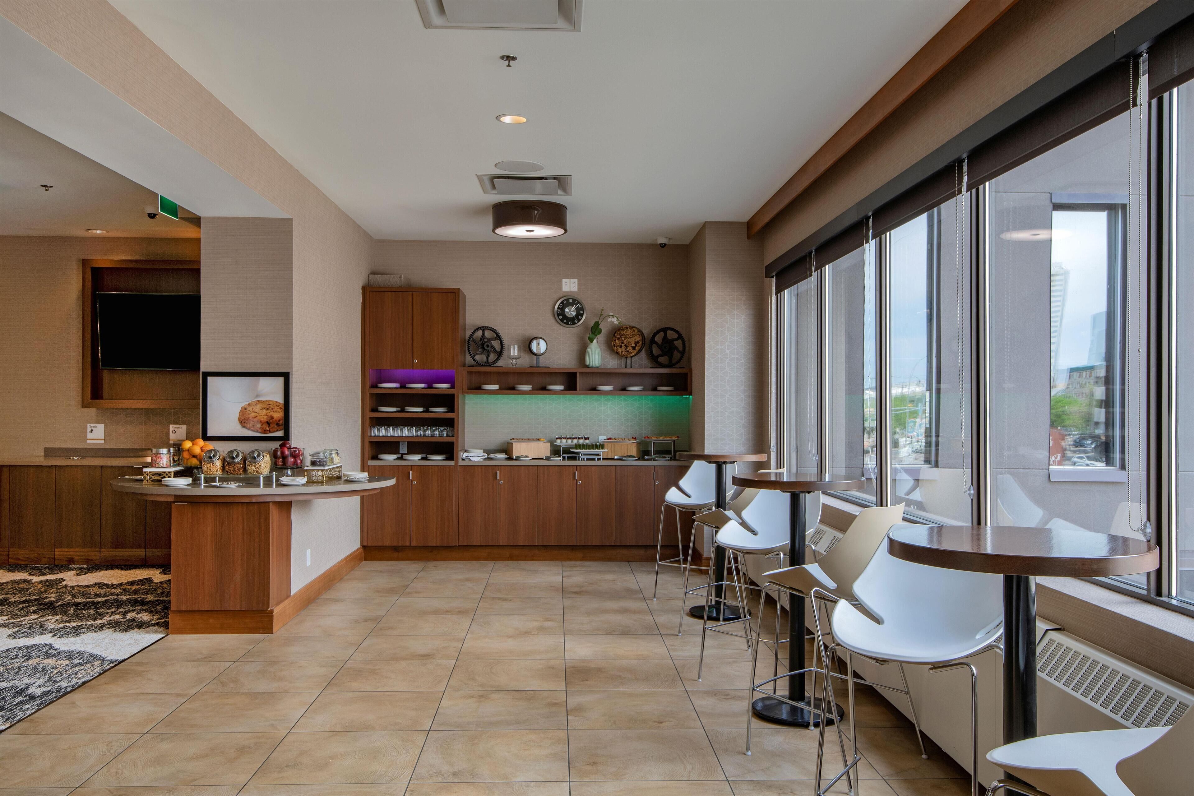 A modern kitchen with a central island, bar stools, and a large window providing a view of the city.