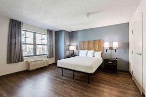 Una habitación de hotel con una cama grande, una mesita de noche con lámparas, una ventana con cortinas y un radiador.