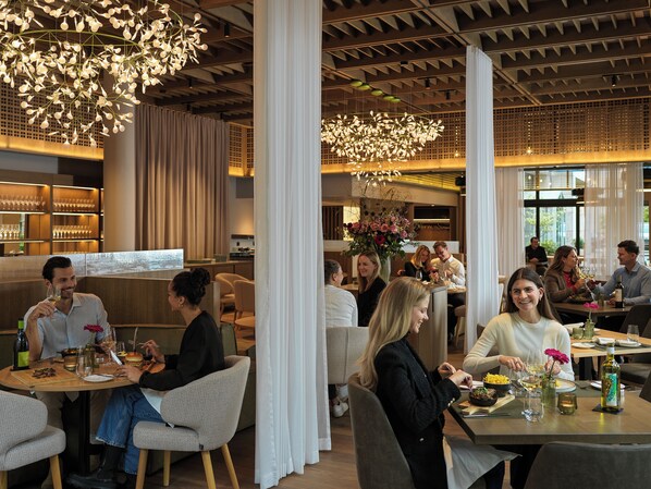 Un interior de restaurante moderno con techos altos, lámparas colgantes y diferentes opciones de asientos, incluyendo mesas y cabinas.