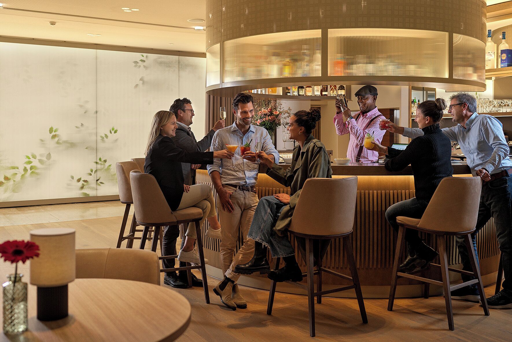 A group of people in a modern bar area with a counter, seating, and a decorative wall with plants.